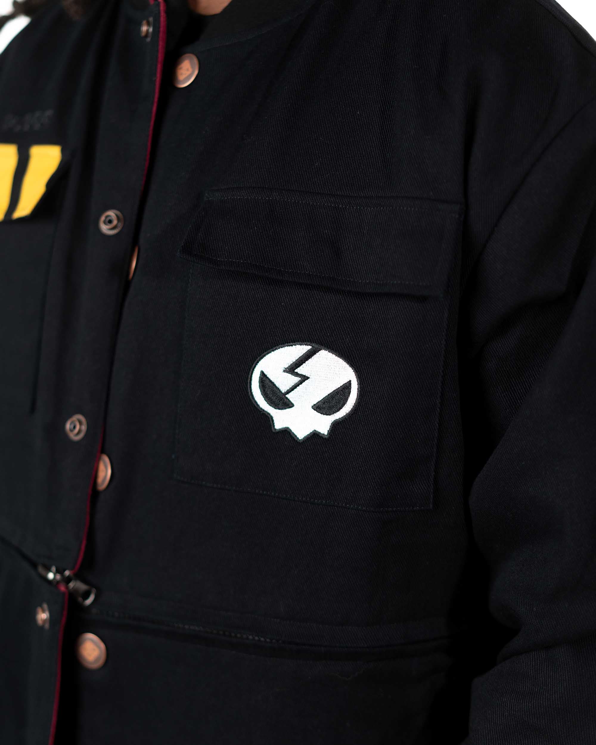 Detailed shot of a male model lifting the snap button flap on the black jacket pocket revealing the skull emblem