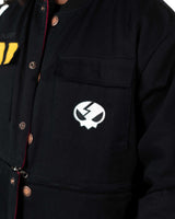 Detailed shot of a male model lifting the snap button flap on the black jacket pocket revealing the skull emblem