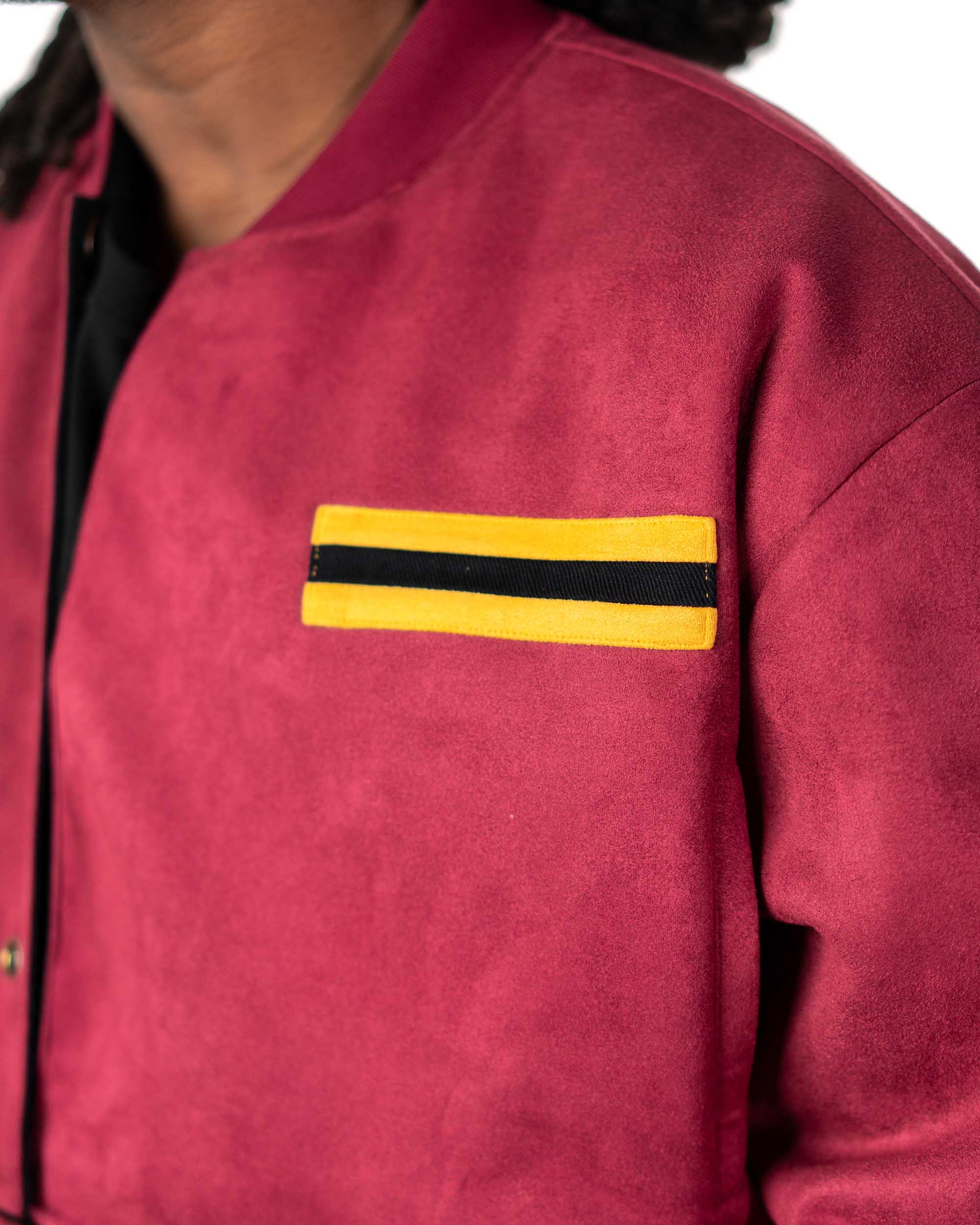 Detailed view of a model placing their hand into the side pocket of the maroon jacket with yellow accents
