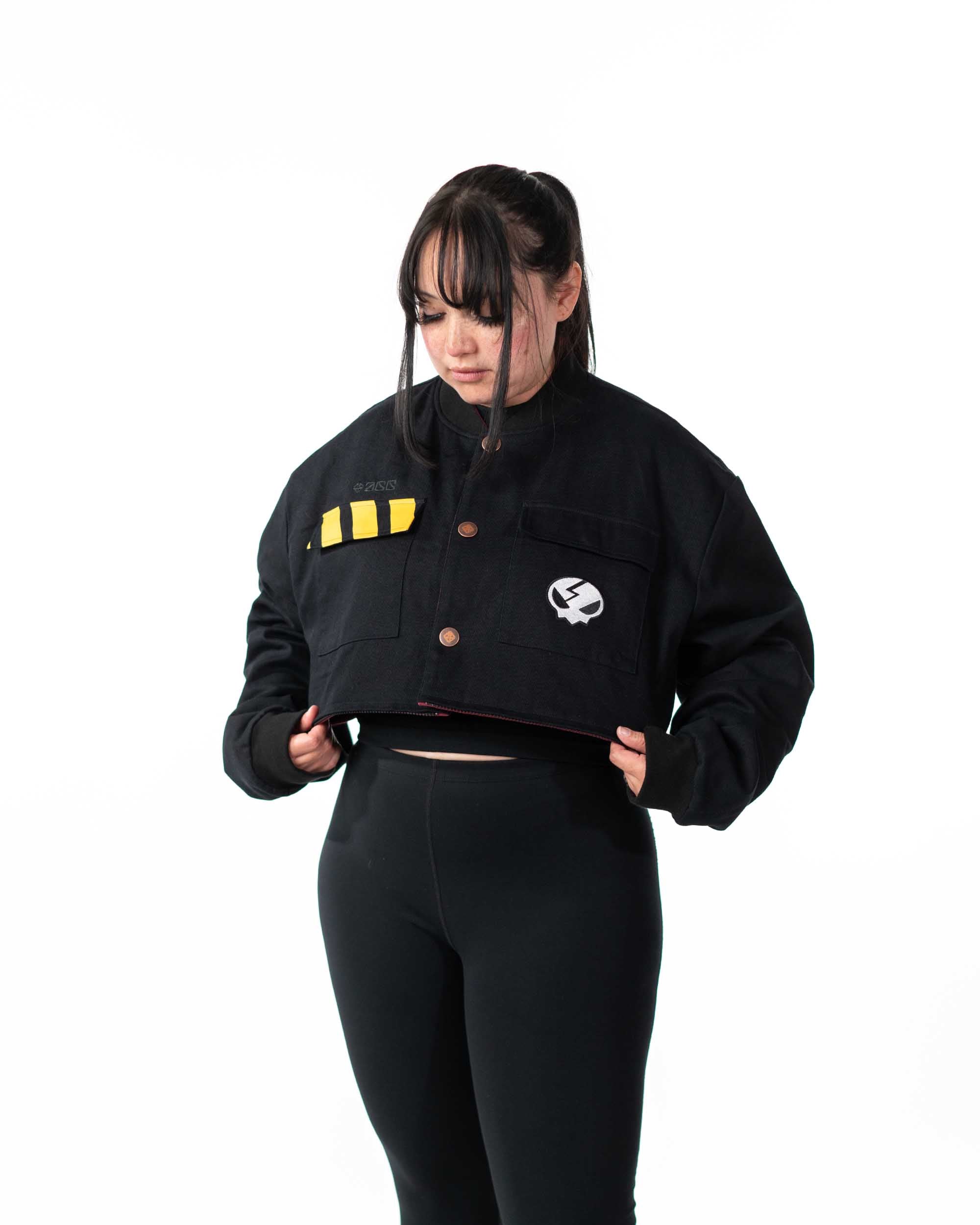 Front view of female model wearing the cropped black side of the reversible jacket with yellow stripe detail