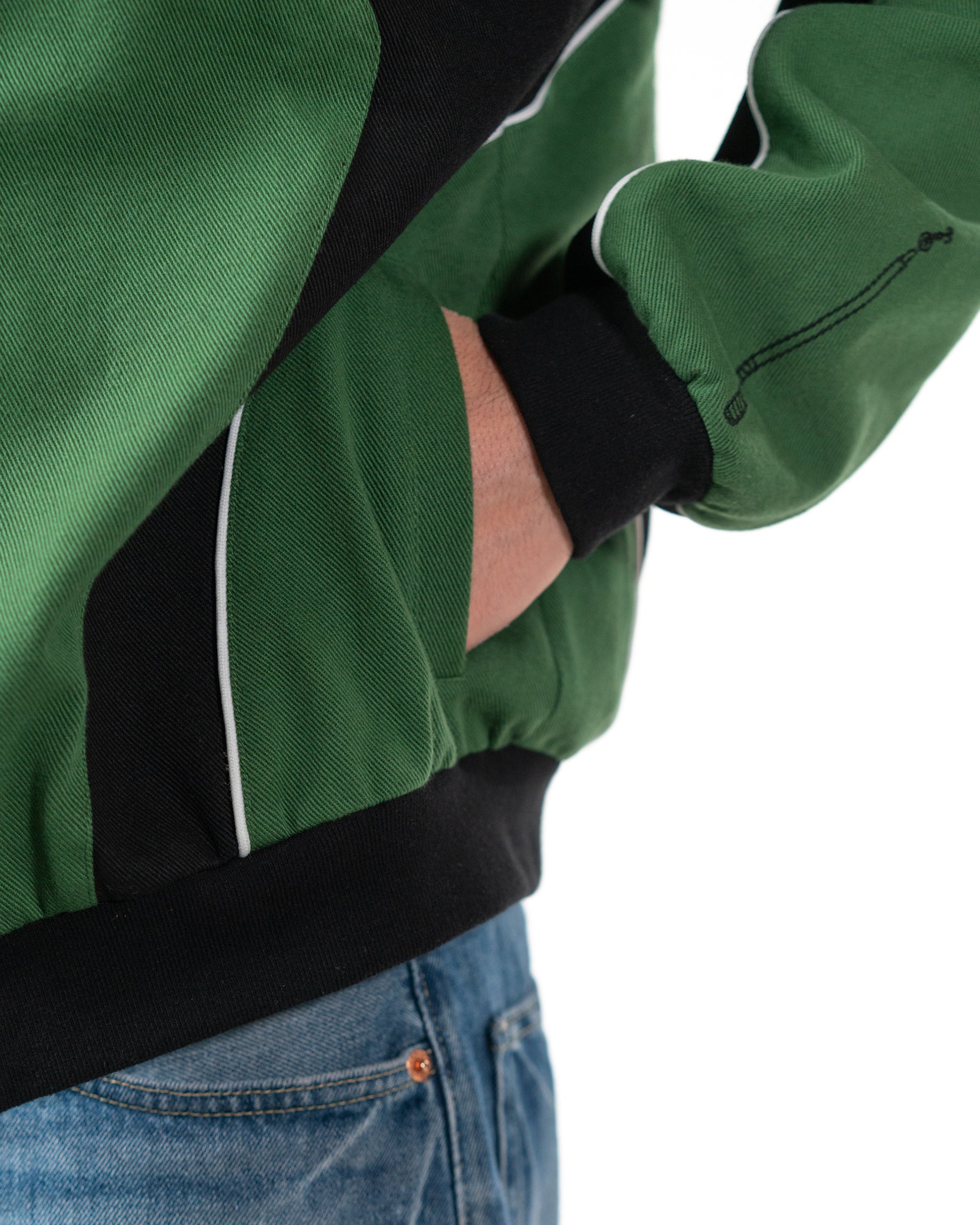 Detailed shot of a model placing a hand inside the lower side seam pocket of the green racing jacket