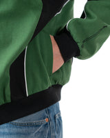 Detailed shot of a model placing a hand inside the lower side seam pocket of the green racing jacket