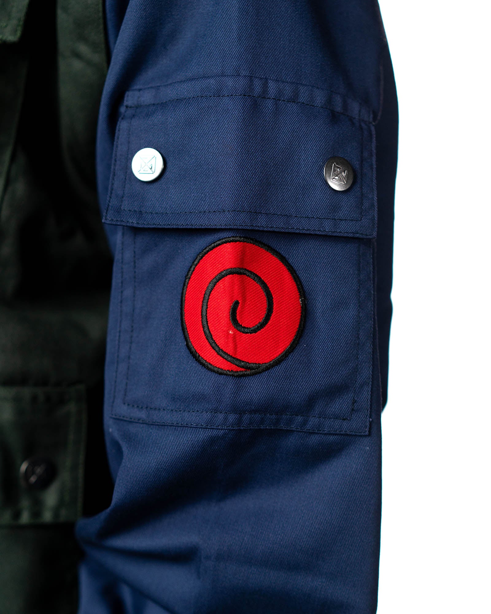 Close-up of the Naruto Shippuden Jonin Jacket navy sleeve pocket with red Uzumaki spiral patch and metal snap buttons