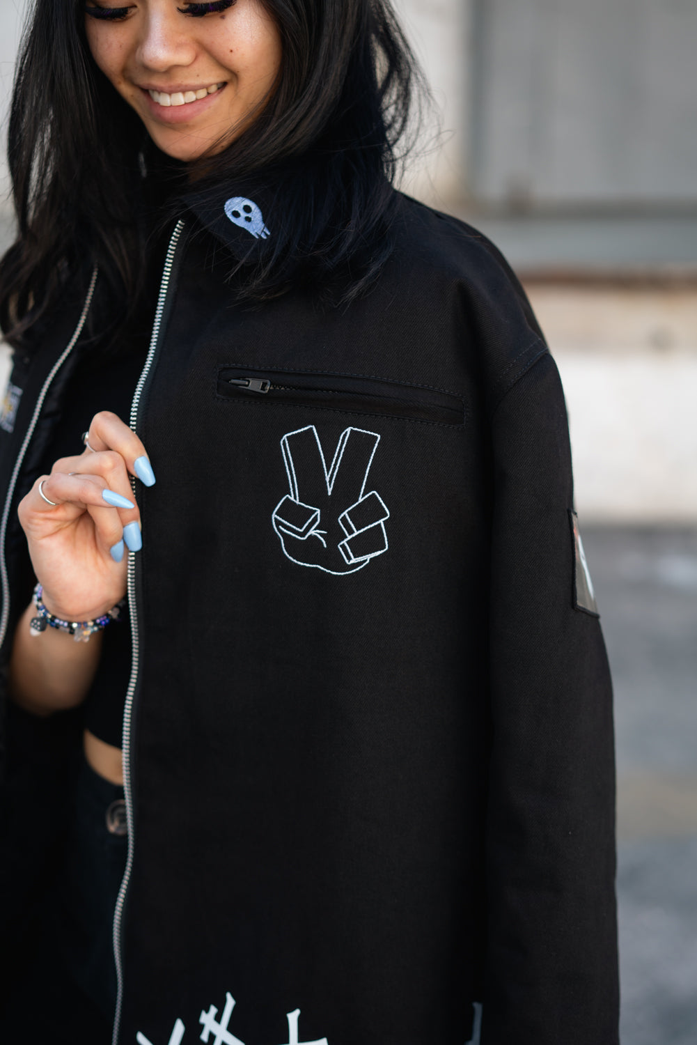 Detail shot of the white Shinigami peace sign hand gesture embroidered on the chest